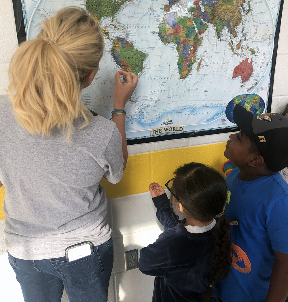 Academy second-grade teacher, Kori Trainor ‘10, and students, Kaylee Trejo and Brandon Marcial Santos, push pins into a map showing the countries represented by students. Photo submitted