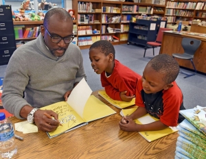 Derrick Barnes signs a copy of his book “Crown: An Ode to the Fresh Cut” for Middle Fork Academy kindergarten students Bradley Stafford (center) and Marlon Nelums on Wednesday. Barnes is a winner of the John Newbery Medal and the Caldecott Medal, among other honors.