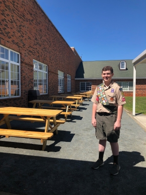 Boy Scout Ryan Porter with the eight picnic tables he and his troop members helped fund, build and install. Porter said Academy at Middle Fork teachers are now using the tables to have outdoor lessons in reading and writing. Photo submitted